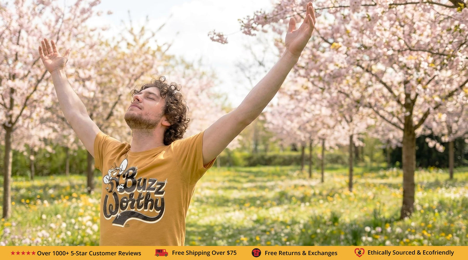 Person wearing a yellow 'Buzz Weathy' shirt with arms raised in a cherry blossom garden