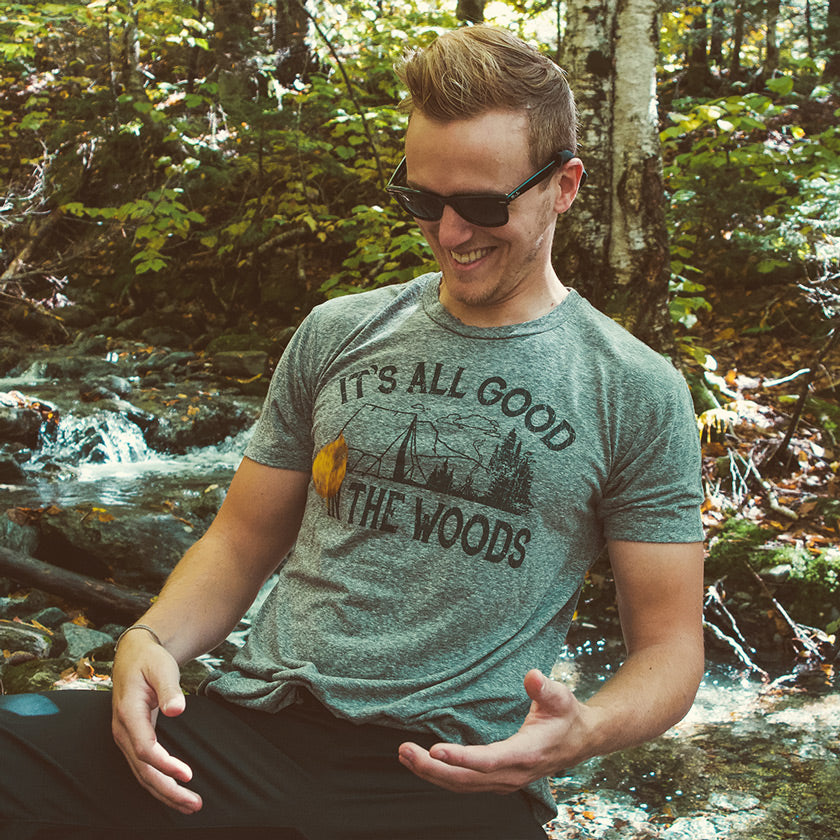 Man wearing a vintage-inspired Solid Threads graphic tee catches a falling autumn leaf beside a wooded stream.